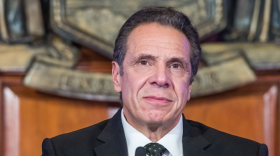 A bust shot of Gov. Andrew Cuomo wearing a gray suit, white shirt, gray spotted tie and gold pin on his lapel