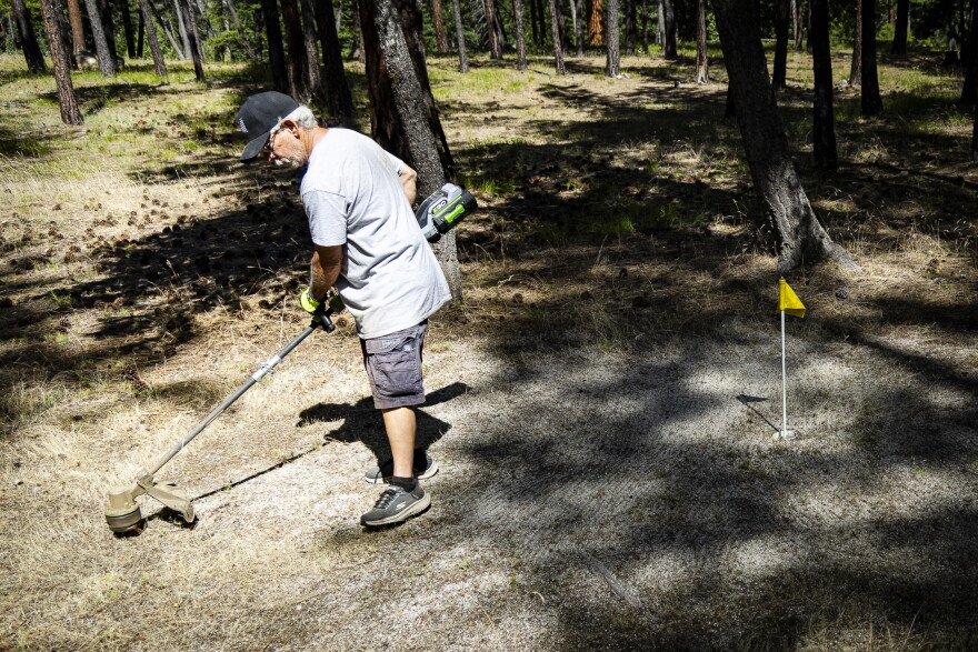 Yellow Pine Fire Chief Tim Rogers weedwhacks one of the town golf course’s greens before the 4th of July tournament.