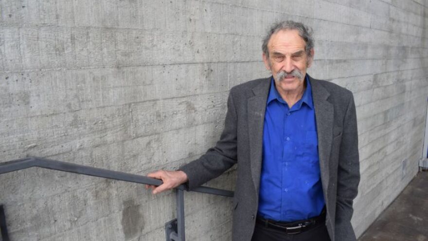 An older man with a large mustache stands on a set of stairs.