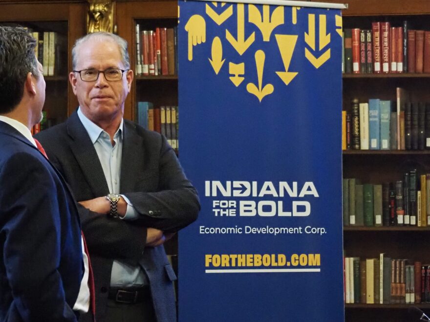 The governor is standing next to a sign that says Indiana for the Bold