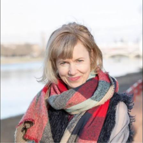 A woman with short blonde hair wears a red, white, and blue scarf and smiles at the camera. 