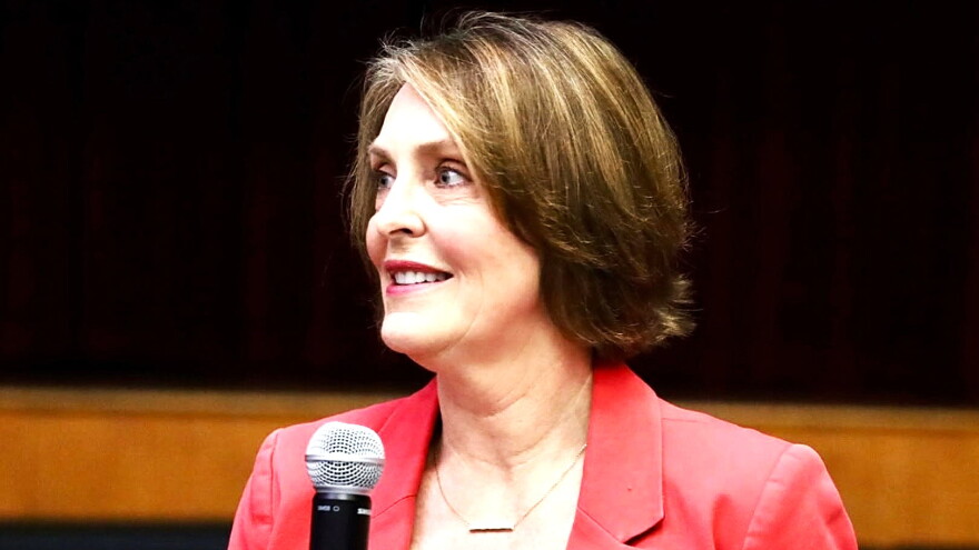 woman with short hair in peach-orange blazer holding microphone 