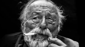 A black-and-white photo of an old man with a cigarette in his mouth. 