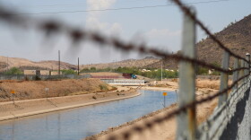 shimmering water flows through a canal in the desert behind a barbed wire fence