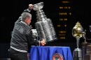 A man holds the Stanley Cup, a giant silver trophy, on a blue table.