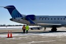 Two men dressed in neon yellow and orange walk towards the back of a United Airlines aircraft parked at the gate. 