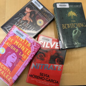 Four library books arranged on a wooden table: Anita de Monte Laughs Last, The Seventh Veil of Salome, Silver Nitrate and The Bewitching.