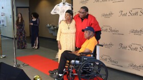 A woman and two men pose for a picture on a red carpet in front of a backdrop that says "Fort Scott Stories."