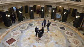 Tourists mill in center of Wisconsin State Capitol and point upwards at the dome.