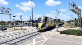 a yellow and black brightline train goes through a railroad intersection