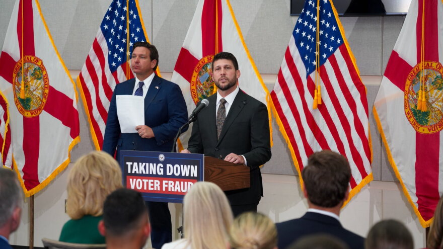 Two men in suit and ties by podium that reads "Taking Down Voter Fraud." A bunch of flags are behind them 