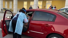 A nurse in PPE reaches into a patient's car to give her a flu shot.