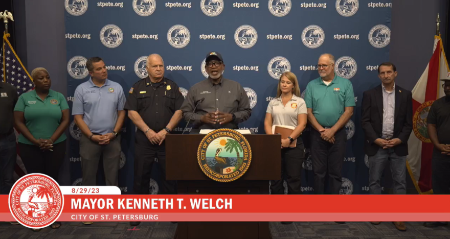 St. Petersburg Mayor Ken Welch in front of a podium surrounded by county officials.