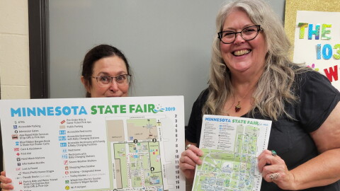 Two people holding maps to the Minnesota State Fair - one map is huge, the other small