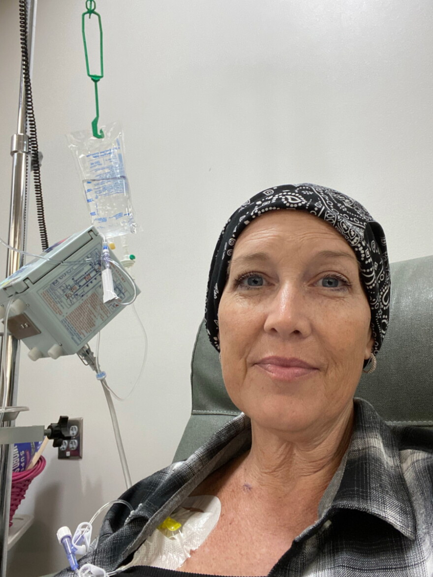 Jennifer George sits in a bed connected to different hospital machines wearing a black bandana.