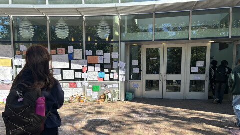 A student stands outside the Batten Arts and Letters building at Old Dominion University on Oct. 26, 2026, looking at signs and other tributes left as a memorial for a student who died at the building the week before.