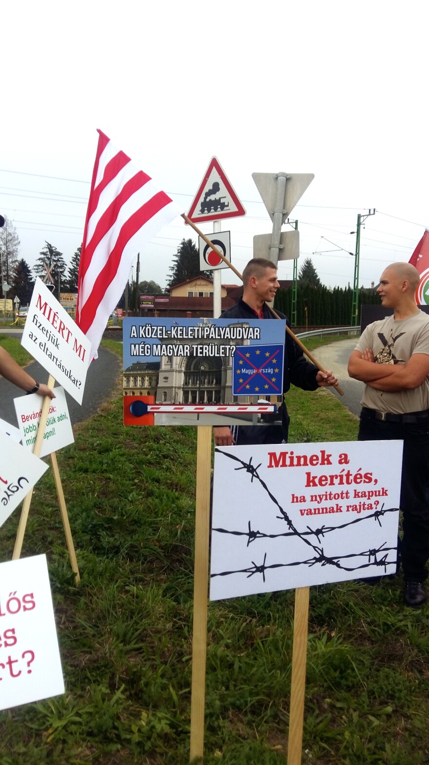 Anti-immigrant placards at a Jobbik rally read "Why have a fence if the gates on it are open?" (lower right) and "Is this a Middle Eastern train station or is it Hungarian?" (center).