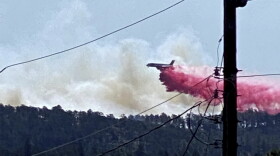 This photo provided by the Village of Ruidoso shows a fire fighting air tanker dropping fire retardant across the mountains near the Village of Ruidoso, N.M., on Wednesday, April 13, 2022. Officials say a wildfire has burned about 150 structures, including homes, in the New Mexico town of Ruidoso. (Kerry Gladden/Village of Ruidoso via AP)