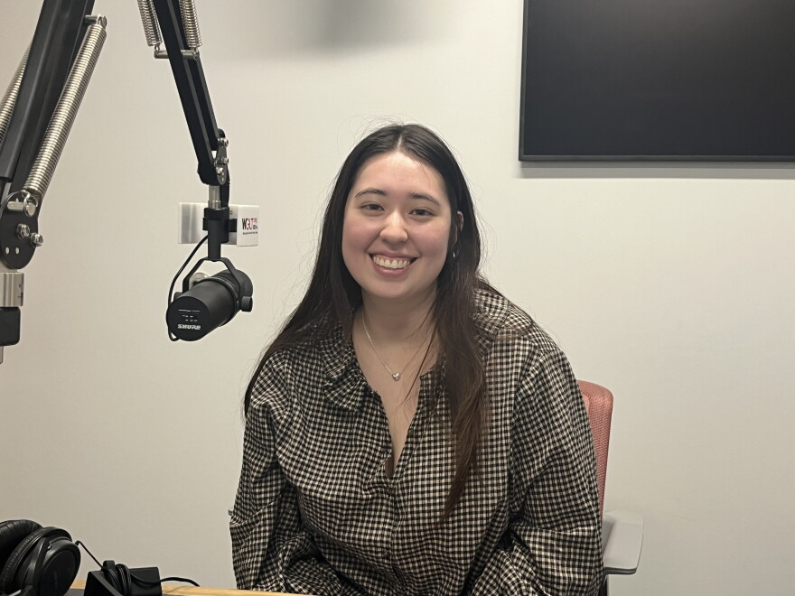 A woman sitting before a microphone. She has brown hear and is wearing a checked shirt. She is ISU graduate student Bridget Nakamura. 