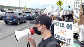A stream of cars drive slowly down Solar Street south of Destiny Mall engaging protestors in solidarity against White House priorities.