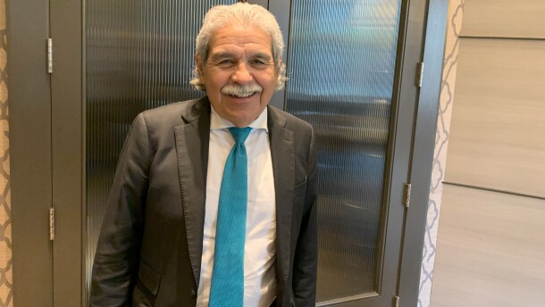 Smiling man, standing, wearing dark suit, turquoise tie and jacket