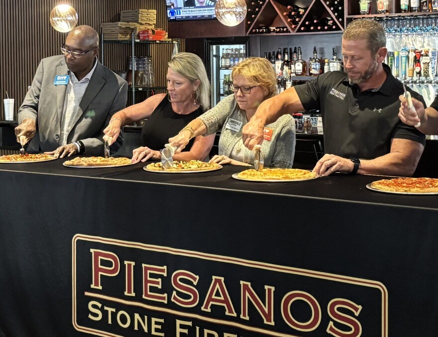 Staff and guests participate in a ceremonial pizza cutting at Piesanos Stone Fired Pizza on West Unviersity Avenue on March 30, 2026. (Alannah Peters/WUFT News)
