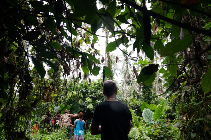 Jon O'Neill walks through a coconut plantation with a group of local residents. To fill in gaps in his knowledge about his late father's life, he says, "I have to see what the sky looks like, what the ground looks like, what the people look like."