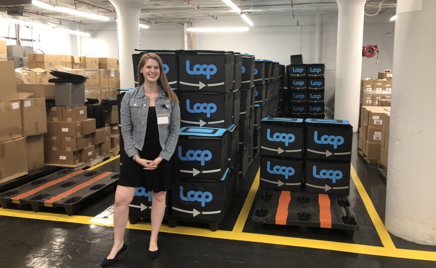 TerraCycle's Heather Crawford stands next to boxes of tote bags for a pilot project called Loop. The bags are filled with products in reusable containers and mailed to customers, who then return the bags and empty containers to be cleaned and refilled.