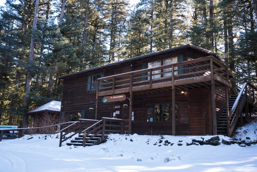 The Fort Abercrombie ranger station under a light blanket of snow in March 2026. It is a two story building with dark brown siding and green accents on the windows. Behind the station, sun filters through spruce trees.