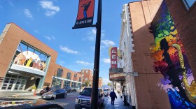 Wide angle photo of a city street. On the right side is a colorful mural depicting a person playing a saxophone and a sign for the Gem theater. On the left is a brick facade  of the American Jazz Museum and Negro Leagues Baseball Museum.