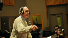A man wearing a cream colored sweater standing at a conductors podium.