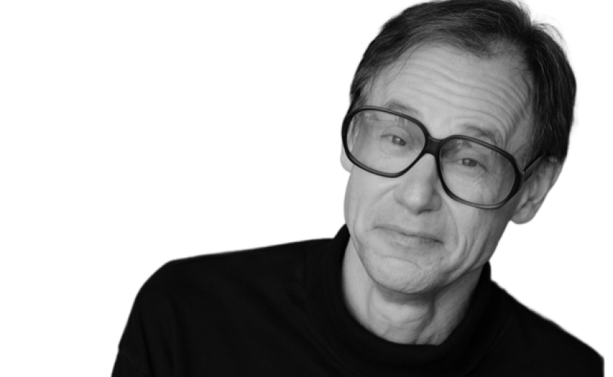 A black and white photo of a man with dark hair who is wearing a dark shirt and eyeglasses.
