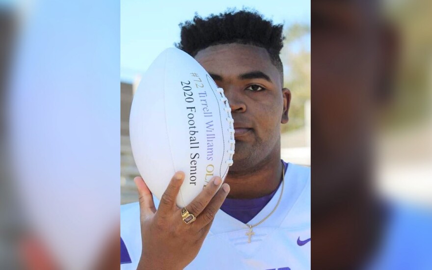 A young Black man wearing a football jersey holds a football vertically, partially blocking his face. The football reads: #72 Tirrell Williams, 2020 Football Senior."