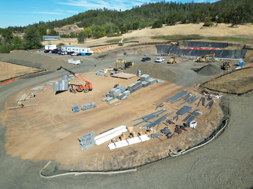 An overhead view of a dirt construction site is shown, with piles of materials as well as construction vehicles. 
