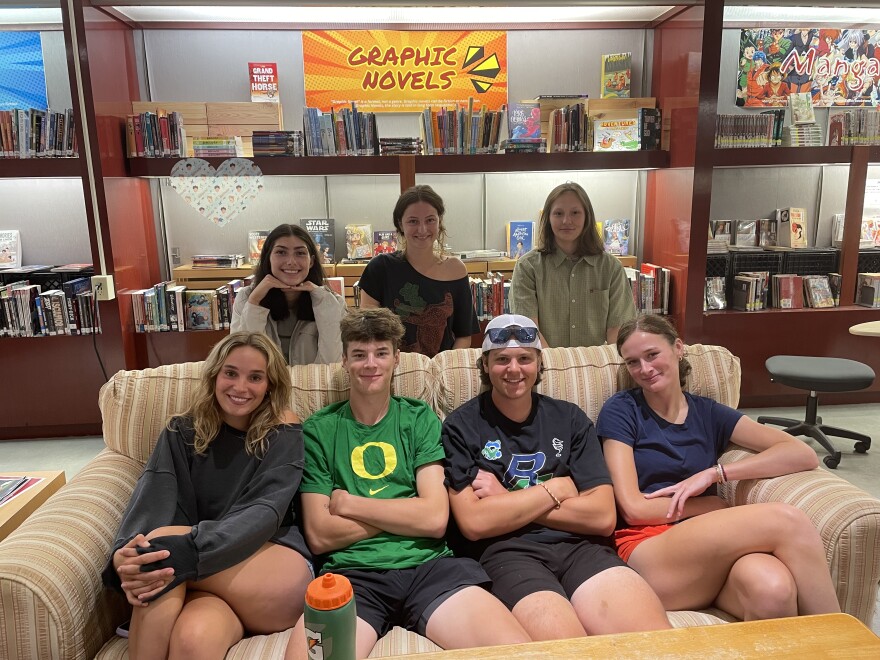 Seven students pose for a picture in front of books in a high school library.