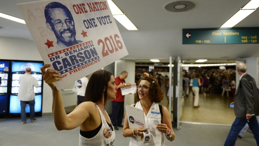 Ben Carson volunteers hold campaign banners and a clipboard as they direct supporters at a rally in Anaheim, Calif.