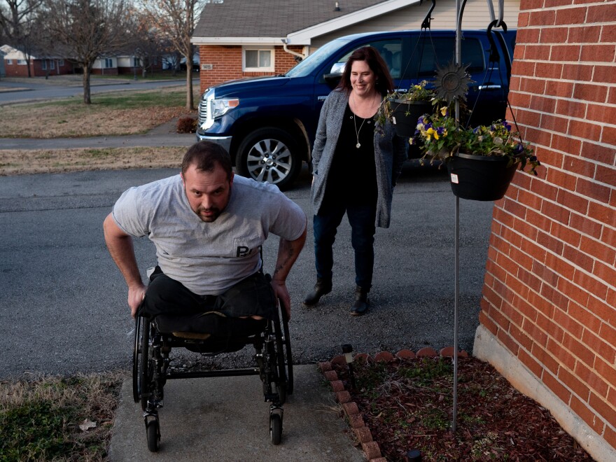 Retired Sgt. Chris Kurtz wheels himself up to his front door as his wife and caretaker, Heather Kurtz, follows behind. The Department of Veterans Affairs told him last summer that he no longer needs a caregiver.