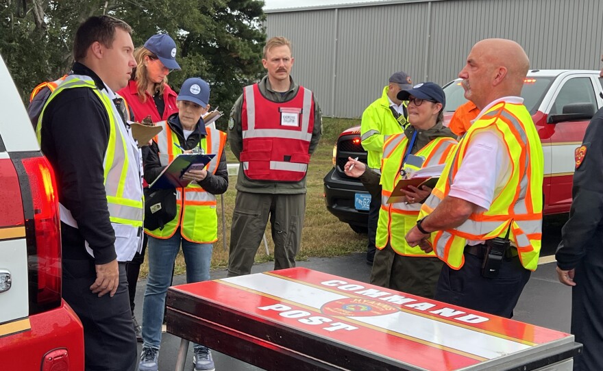 Incident commander John Puleo, left, a lieutenant at the Hyannis Fire Department, updates Airport Manager Katie Servis (in blue hat, at right) and other participants in a full-scale emergency drill at Cape Cod Gateway Airport in Hyannis, Sept. 26, 2024.