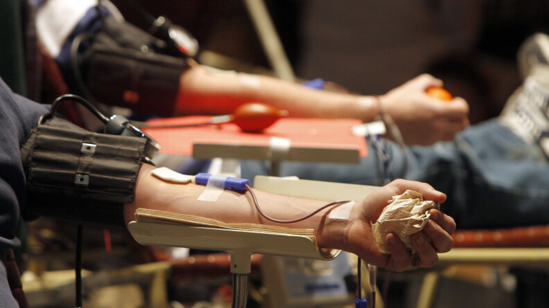 Two people sit in chairs donating blood. 