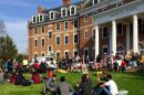 Students sit and stand on a lawn, eating and talking. 