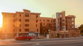 The sun is shining on the construction of an apartment complex as a red truck pulls off the road.