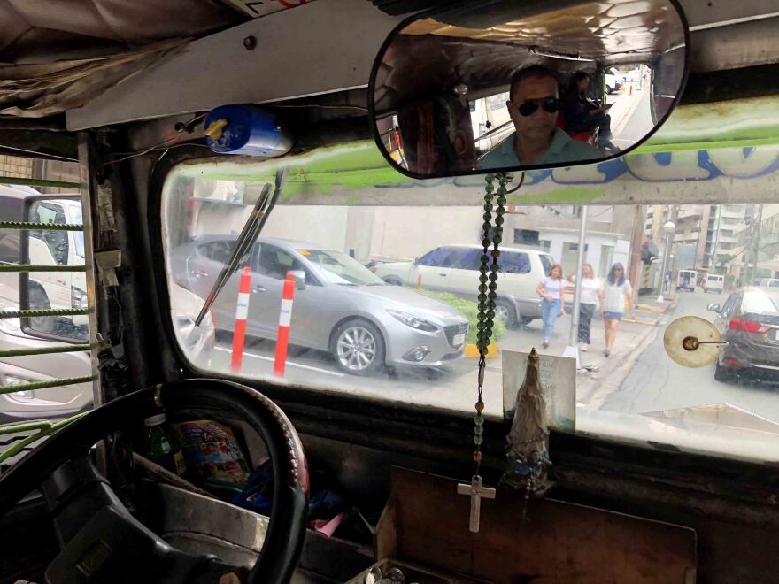 Raffy Solongon (in rear-view mirror), 47, drives his jeepney through Makati City in Manila. He earns about $10 a day and is one of thousands of drivers who say they can't afford the new jeepney model the government wants them to buy.