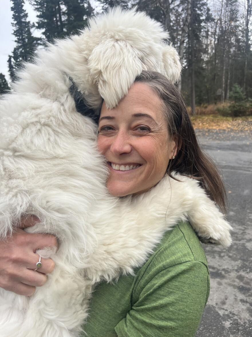 A woman in a green shirt smiles as she hugs an off-white curly-coated dog.