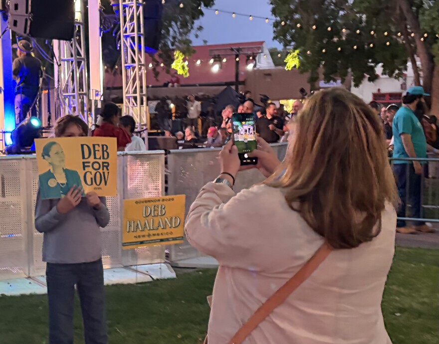 A mother takes a photo of her daughter holding a Deb Haaland campaign sign.