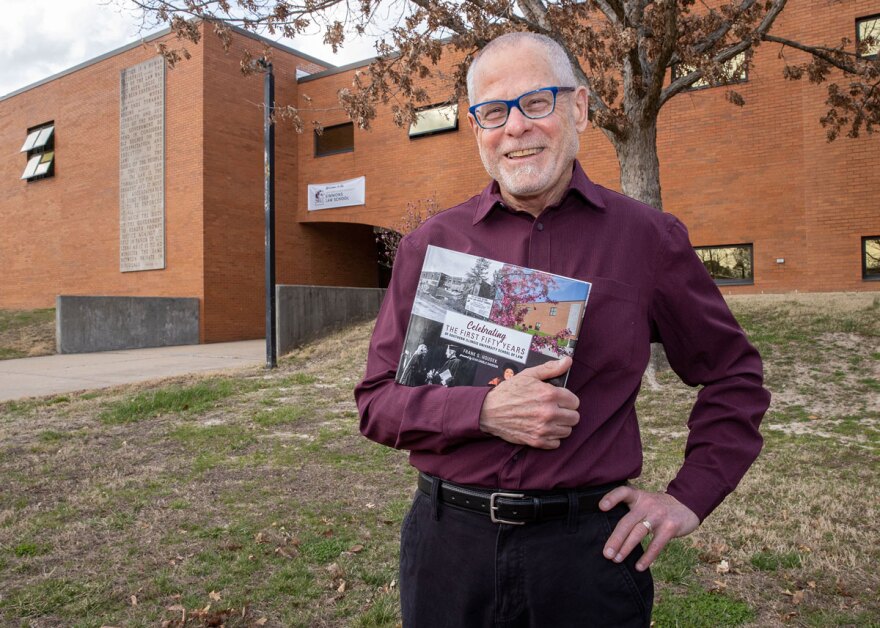 Frank G. Houdek poses with a book in front of a building on campus.