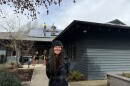 A woman stands smiling in front of a building with solar panels being installed on the roof.
