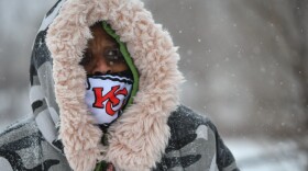 Closeup photo of a woman bundled in a heavy coat with a fuzzy lining watching snow fall around her.