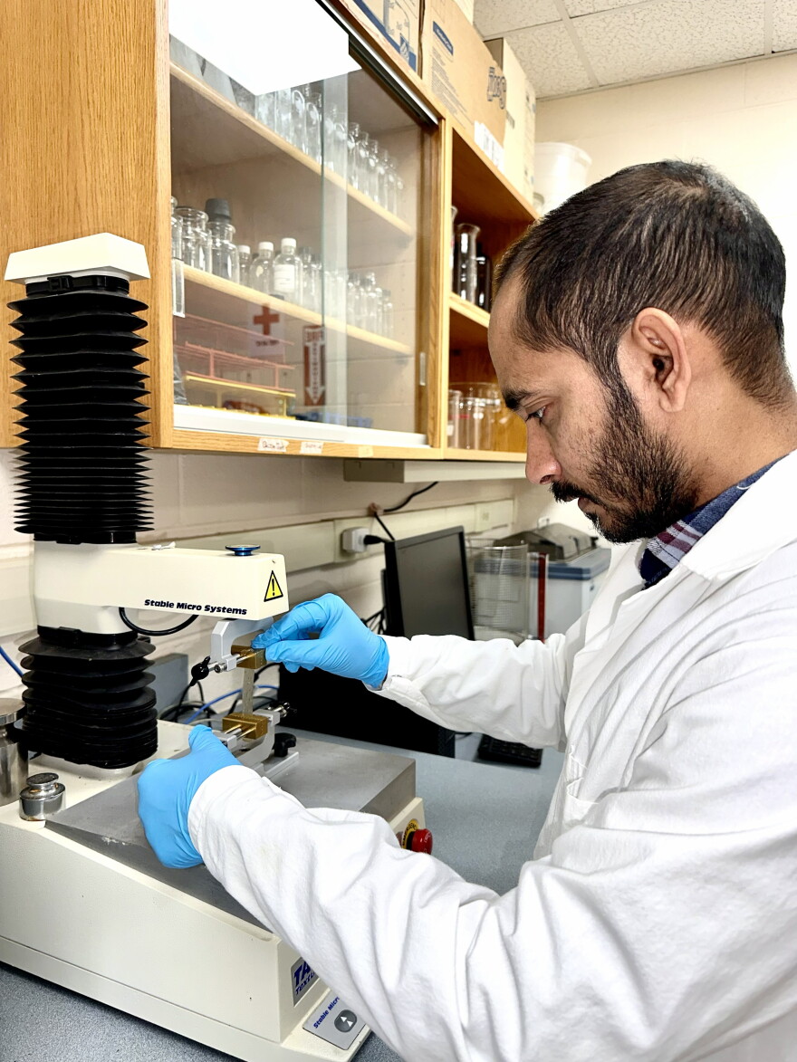 A researcher wearing a lab coat and blue gloves works with testing equipment.