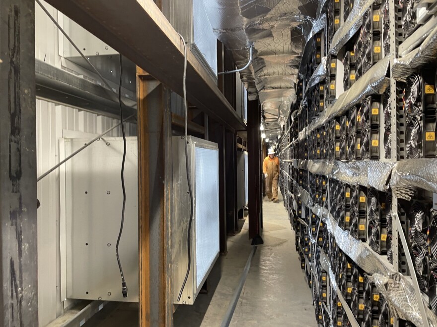 A worker walks down a hallway where machines are running at Blockware Mining.