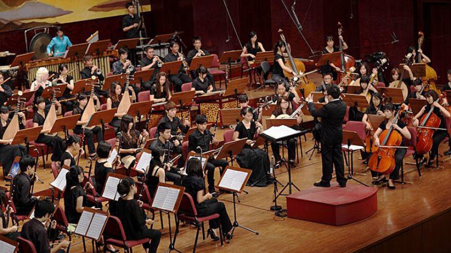 A conductor leads an orchestra on stage.